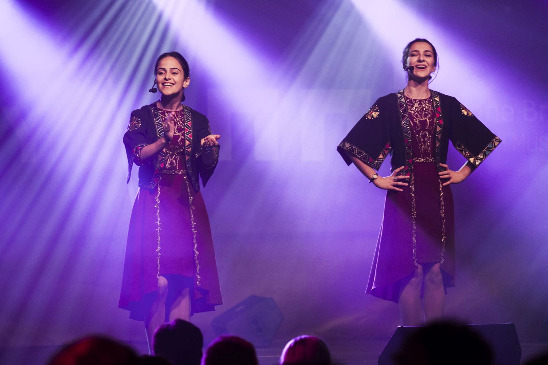 Dwie kobiety w tradycyjnych strojach śpiewają i zabawiają publiczność.