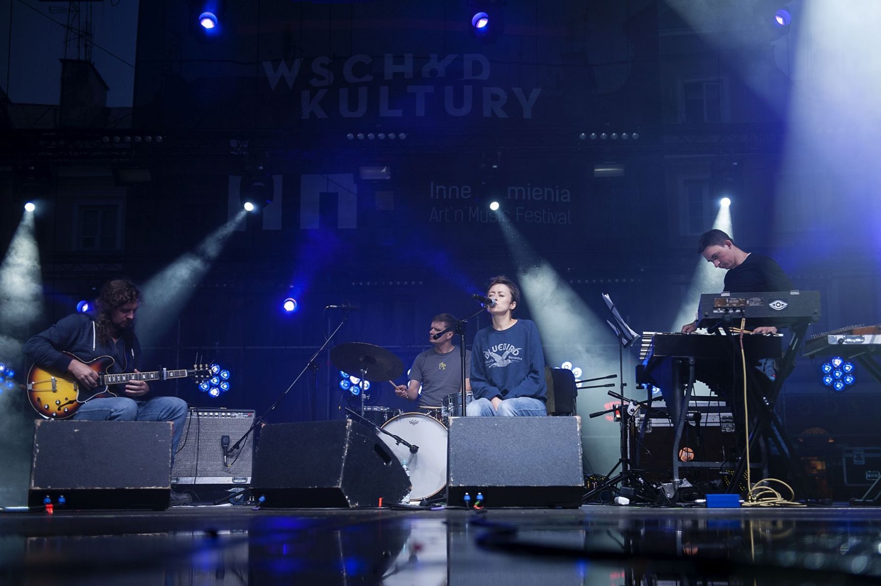 Zbliżenie na scenę. Trzech muzyków gra, a wokalistka śpiewa.