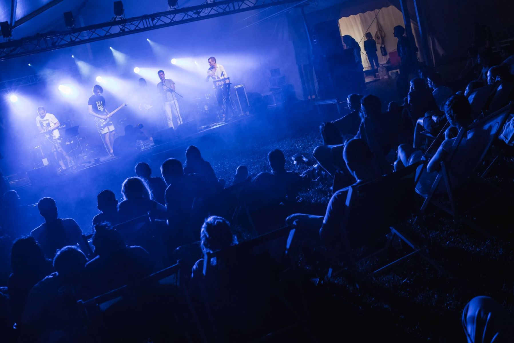 Publiczność słucha koncertu. Ludzie siedzą na leżakach.