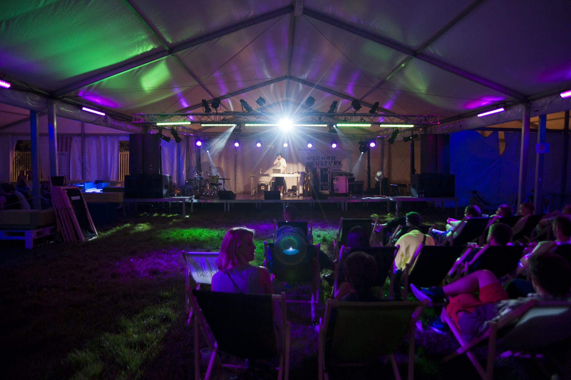 Artysta gra na scenie. Poniżej na leżakach siedzi publiczność.