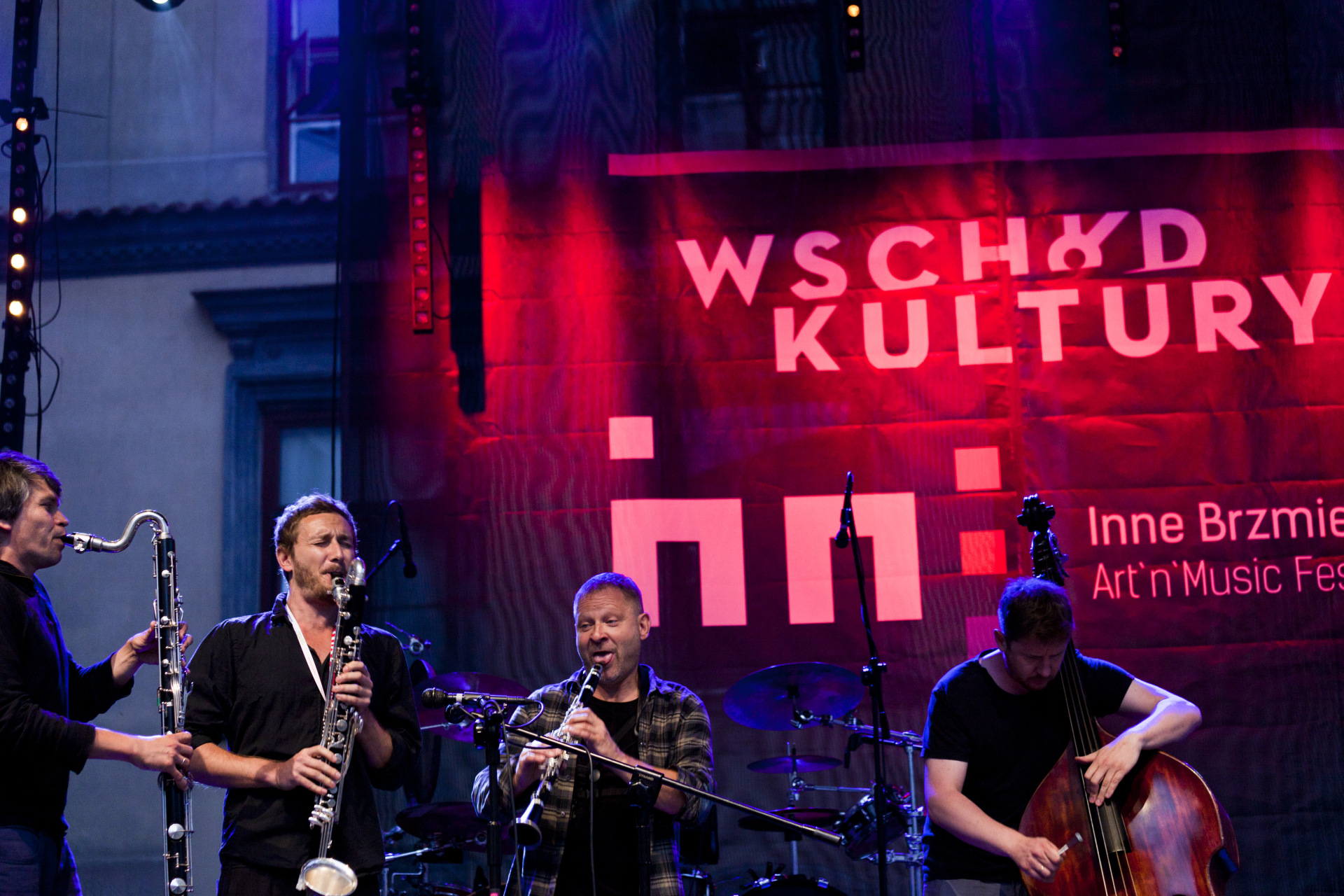 Trzej muzycy grają na instrumentach dętych, a czwarty na wiolonczeli.