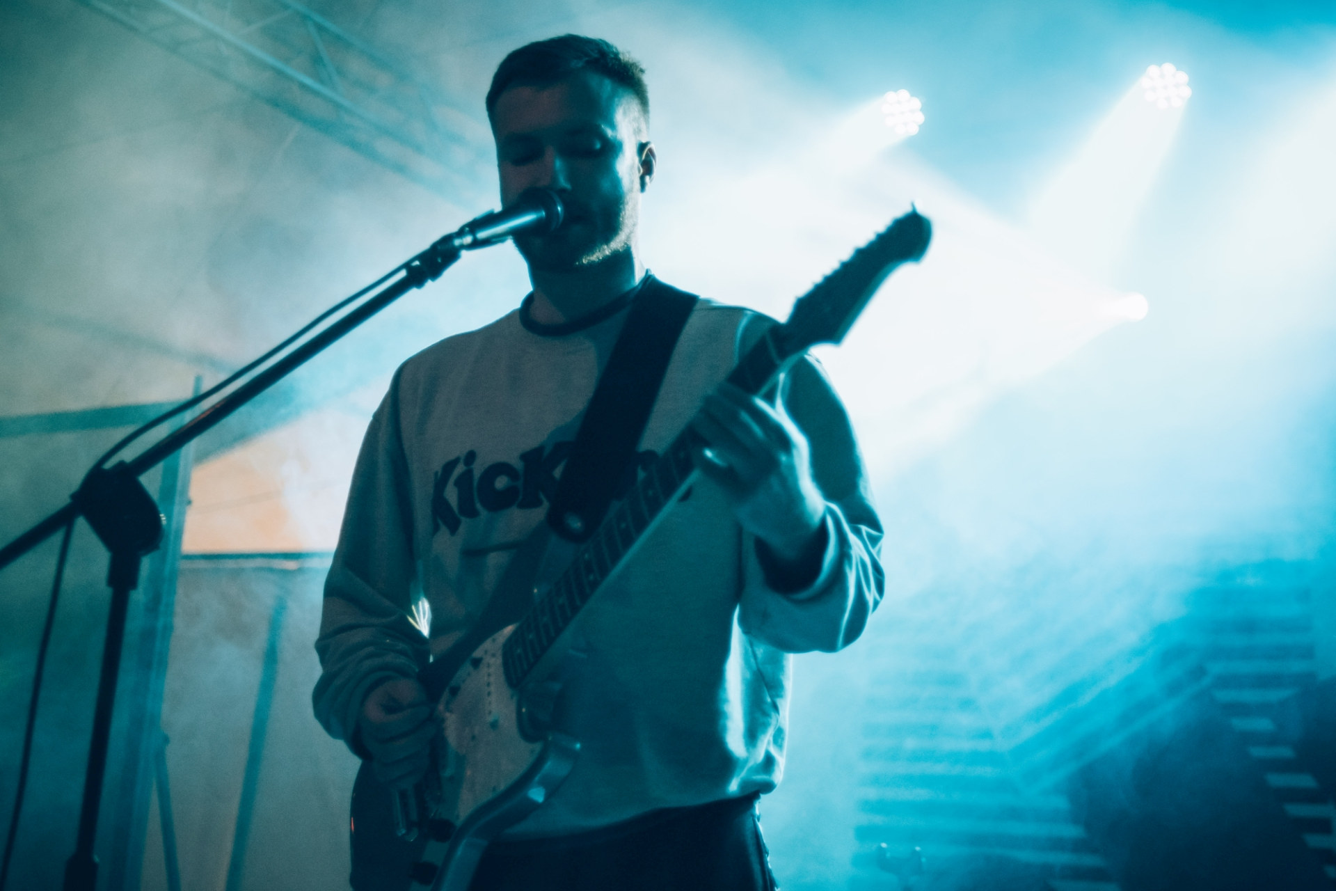 Zbliżenie na wokalistę, który gra jednocześnie na gitarze.
