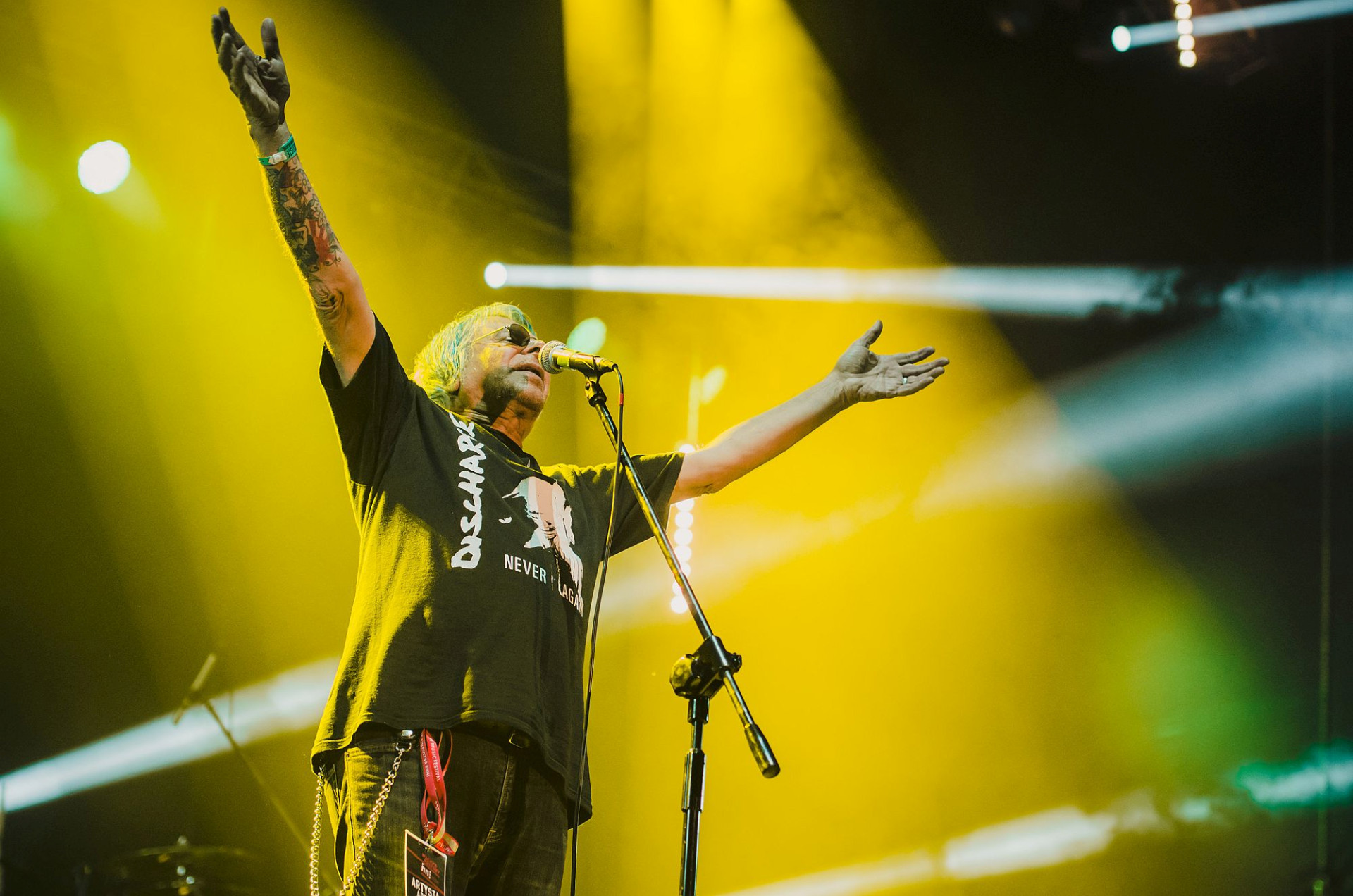 Wokalista śpiewa. Ma ręce uniesione do góry.