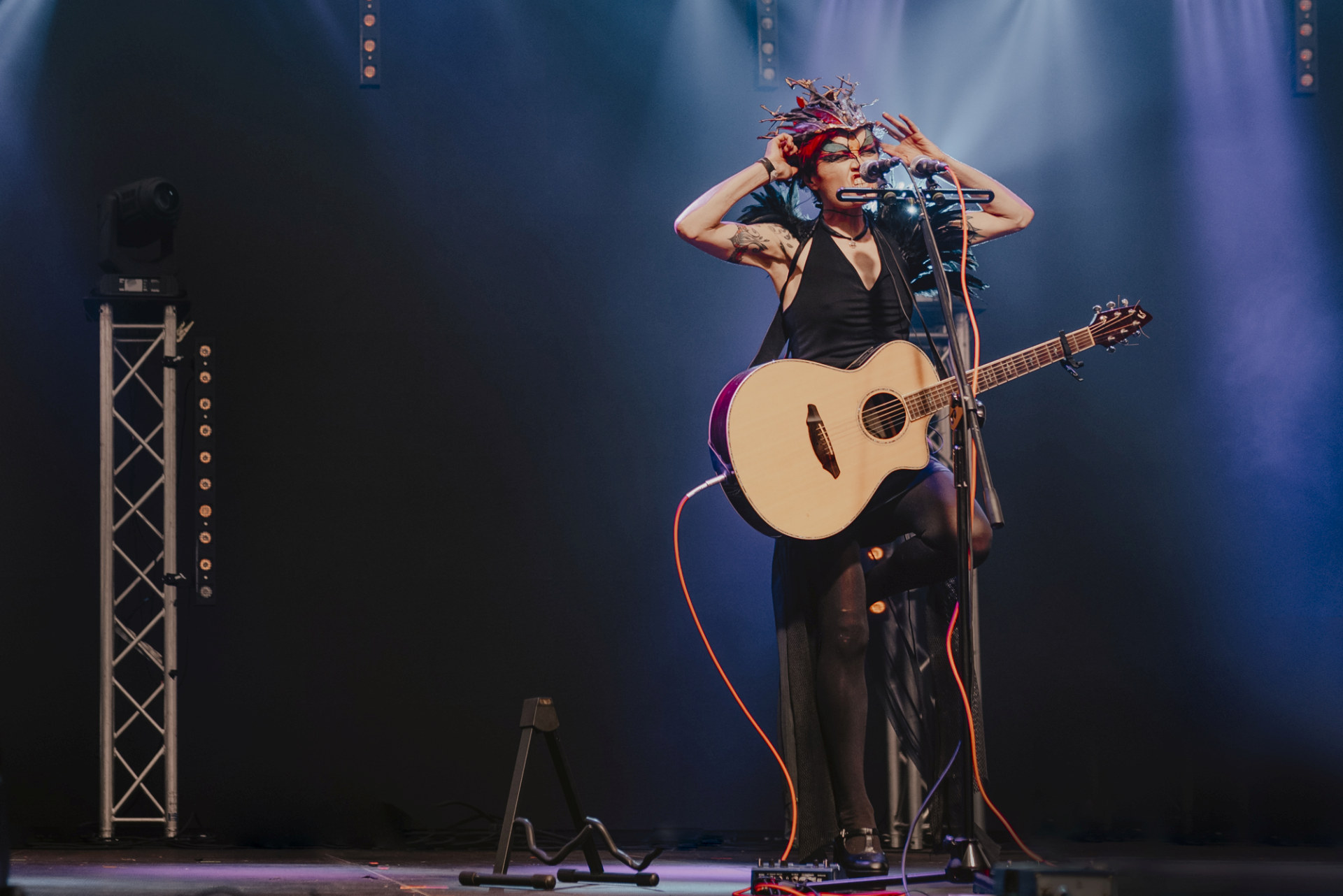 Artystka śpiewa i gra na gitarze. Na twarzy ma maskę karnawałową.