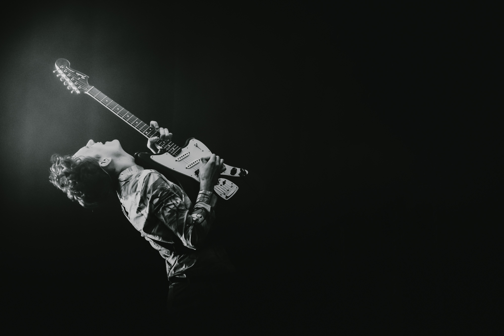 Czarno-biała fotografia. Artysta unosi gitarę do góry.
