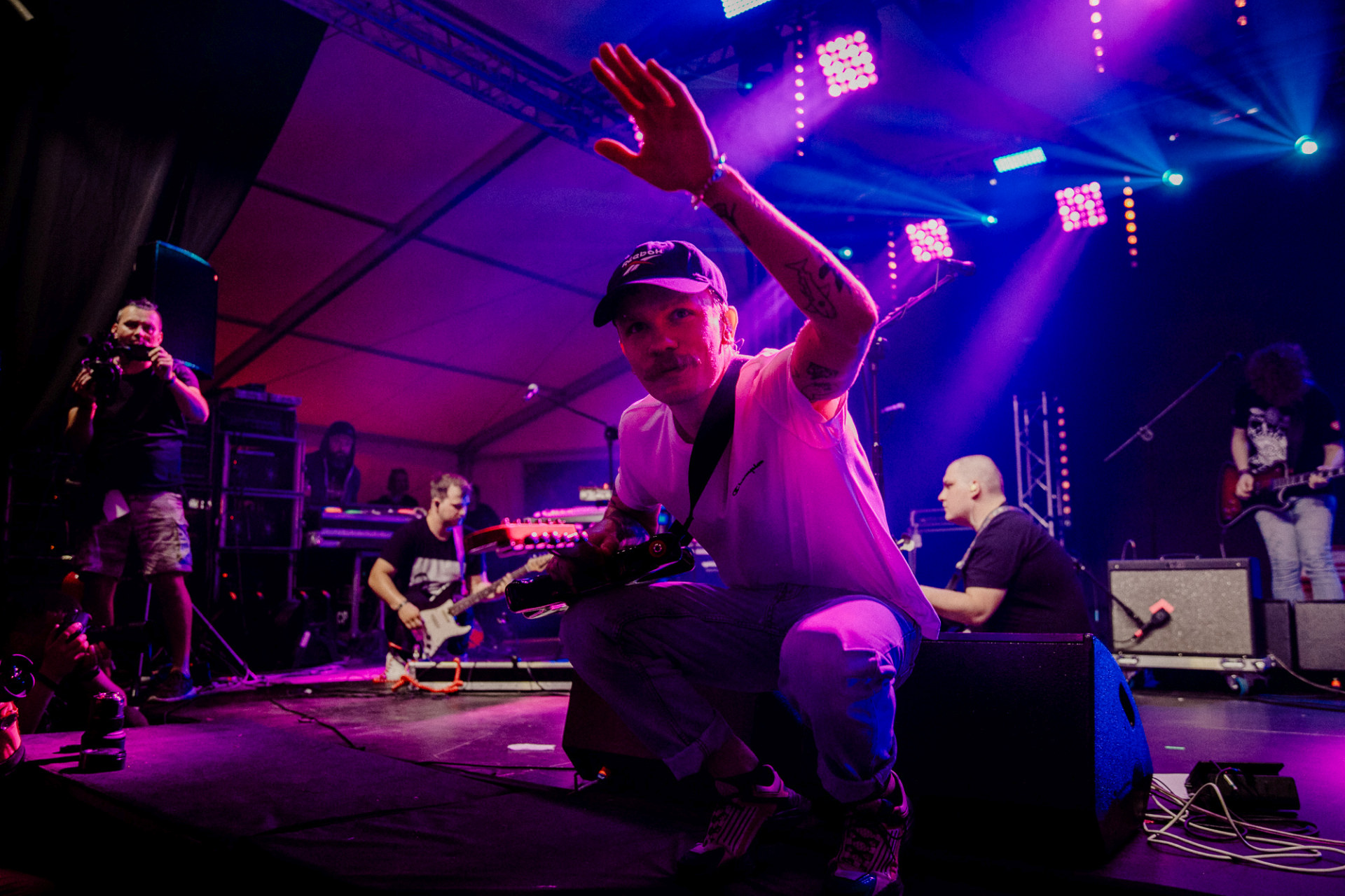 Artysta macha do publiczności. W tle są pozostali muzycy z zespołu.