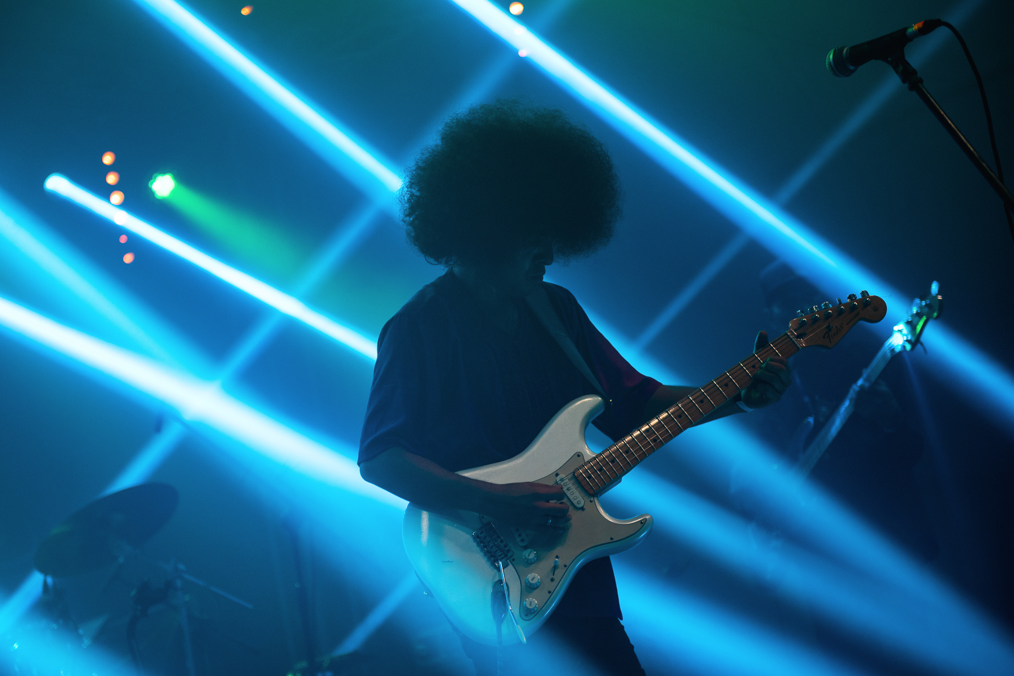 Gitarzysta gra na instrumencie. Mężczyzna ma długie kręcone włosy.